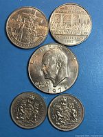 Five coins grouped on blue surface showing obverses and commemorative reverses