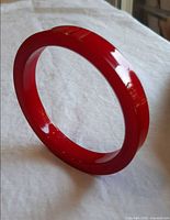Red Bakelite bangle standing upright to show overall shape and finish