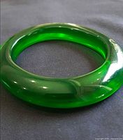 Full view of translucent green lucite bangle bracelet on fabric background