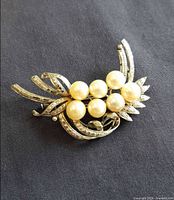 Full view of silver-tone brooch showing six faux pearls and rhinestone scroll design