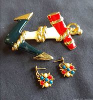 Anchor pin and both earrings together on dark fabric background