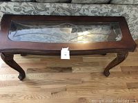 Top front view showing glass inset rectangular top with wooden frame and carved legs.