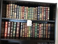 Top two shelves of bookcase showing leather bound volumes in multiple colors with gold gilt decorations and titles