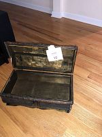 Small open antique-style black and gold wooden treasure chest on a wooden floor