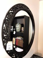 Round ornate carved wood framed mirror facing bookshelf.
