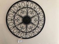 Front view of round black metal wall decor with intricate design and circular frame
