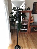 Black metal floor lamp shown near window and light-colored wood floor with white frosted glass upward shade.