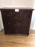 Front view of wooden drawer chest with 9 drawers and dark metal cup handles, showing overall condition and design.