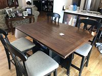 Full view of rectangular table with four bar-stool height chairs arranged around it, showing wooden table top and pedestal base with shelves.