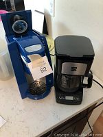 Front and slight angle view of blue Keurig coffee maker and black drip coffee machine on counter.