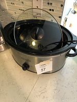 Front angle photo of the stainless steel Crock-Pot slow cooker with glass lid, control knob, and black handles on a kitchen counter.