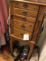 Photo of a five-drawer wooden jewelry dresser with metal handles and legs. Side hooks contain necklaces. Shoes and other items are stored at its base.