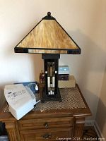 Lamp placed on wooden night-table in room with visible wall and small items around lamp base