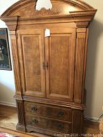 Front view of the wooden bedroom armoire showing the ornate top, two doors, and two drawers.