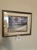 Framed seascape painting with a beach, ocean, and rocky shore under cloudy sky.