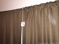 Two brown blackout curtain panels hanging from rod in a room, showing texture and color.