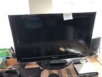 Front view of Sansui flat-screen TV including the remote control placed on the stand