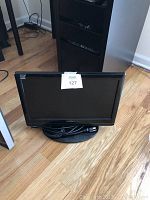 Black Insignia flat-screen television on wooden floor with power cord coiled on stand.