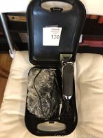 Open black Wahl carrying case showing electric hair clipper inside with coiled power cord in plastic wrap.