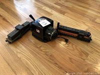 Overview of two Lionel model train engines and black transformer on wood floor.