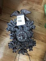 Photo of a dark carved wooden cuckoo clock featuring a bird and oak leaf design around the clock face with Roman numerals