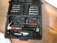 Black plastic case open showing hand tool set including wrenches, sockets, hammer, pliers, screwdriver, and utility knife.