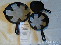 Three cast iron pans with felt protectors and instruction leaflet, top view.