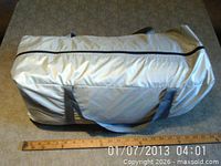 Silver nylon zippered carry bag with gray handles holding tent