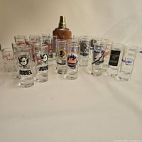 Group of shot glasses with sports logos arranged in front of flask