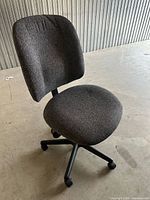 Front three-quarter view of grey fabric armless office chair showing seat, backrest, base and casters