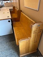 Full view of oak church pew against wall highlighting length and carved end panel with cross