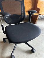 Front angled view of black mesh back office chair with padded seat and casters