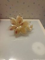 Front view of clear and cream glass flower paperweight with curled stem