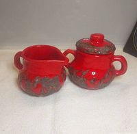 front view of red and black fat lava creamer and sugar bowl with lid