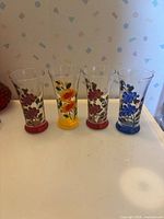 Four floral glass vases lined up showing painted designs and colored bases