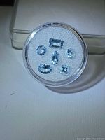 Six faceted aquamarine stones in clear round jar on white background