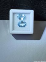 Front view of two faceted oval aquamarines in display box