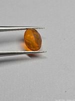 Side view of orange oval faceted gemstone held by tweezers