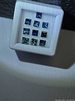 Front view of nine princess cut blue sapphires in display box
