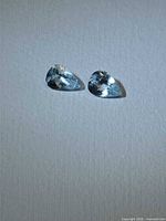 Two light blue pear-cut aquamarine gemstones on neutral background