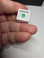 Emerald in display box held between fingers, showing size and color