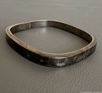 Rounded square sterling silver bangle lying flat on surface