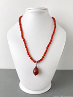 Full view of red-orange gemstone beaded necklace on display bust