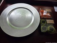 Single silver charger plate beside two boxes of napkin rings