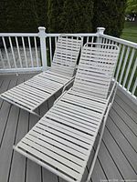 Two white metal chaise lounges with plastic straps on deck