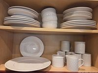 Stacked dinner and salad plates, bowls, mugs, sugar bowl and creamer displayed on shelf