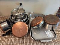 Grouped view of two copper-bottom saucepans, food mill, three nesting bowls, roasting pan