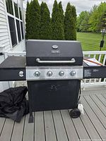 Full view of grill on deck with cover draped left side and propane tank mount visible