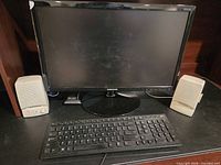 Front view of Samsung monitor flanked by two Optimus speakers and keyboard on desk
