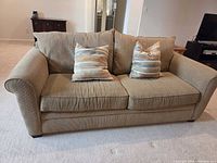 Front view of taupe fabric loveseat with two striped pillows